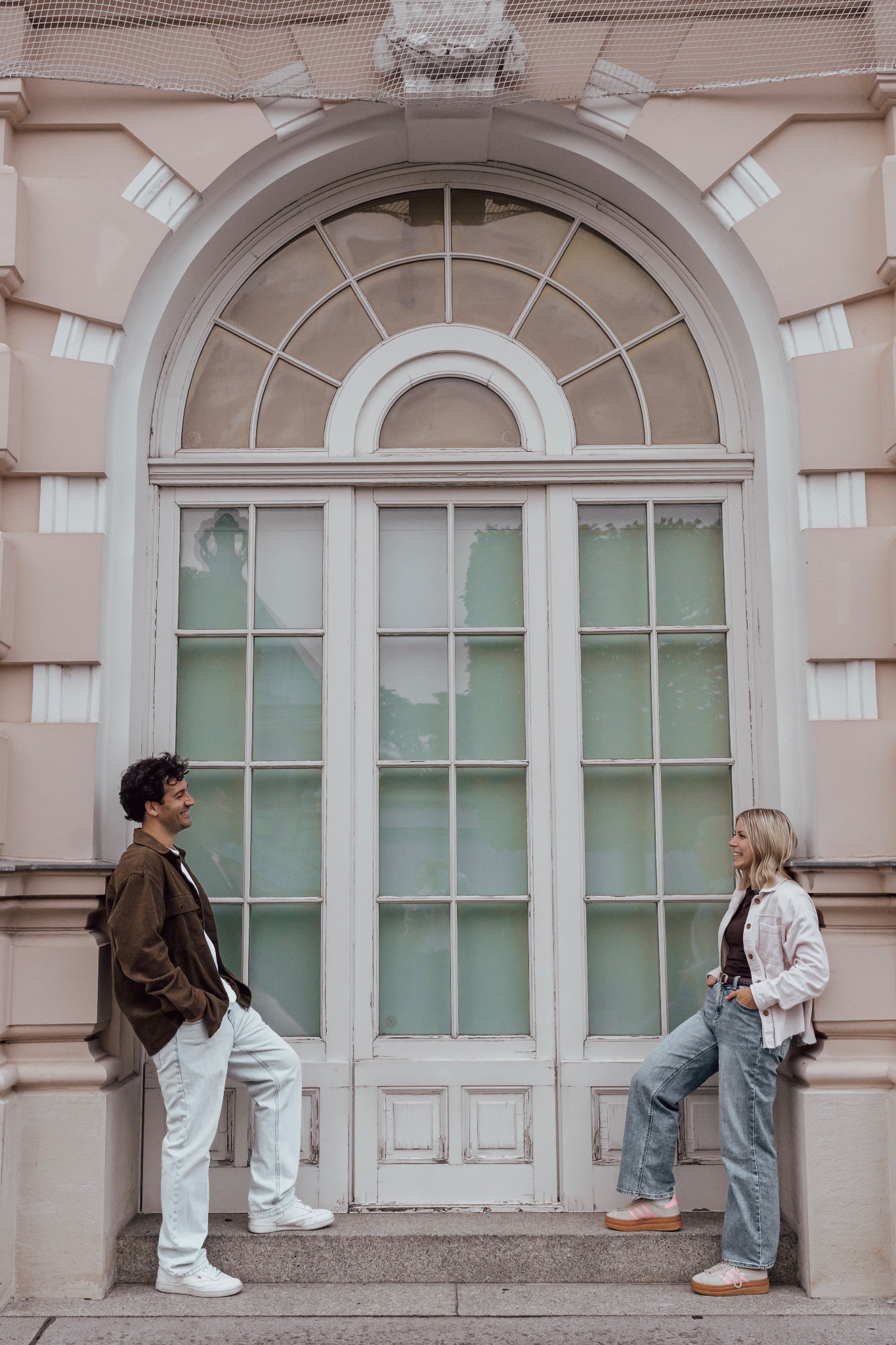 Young couple standing on opposite sides of glass doors at the Albertina in Vienna, looking at each other.