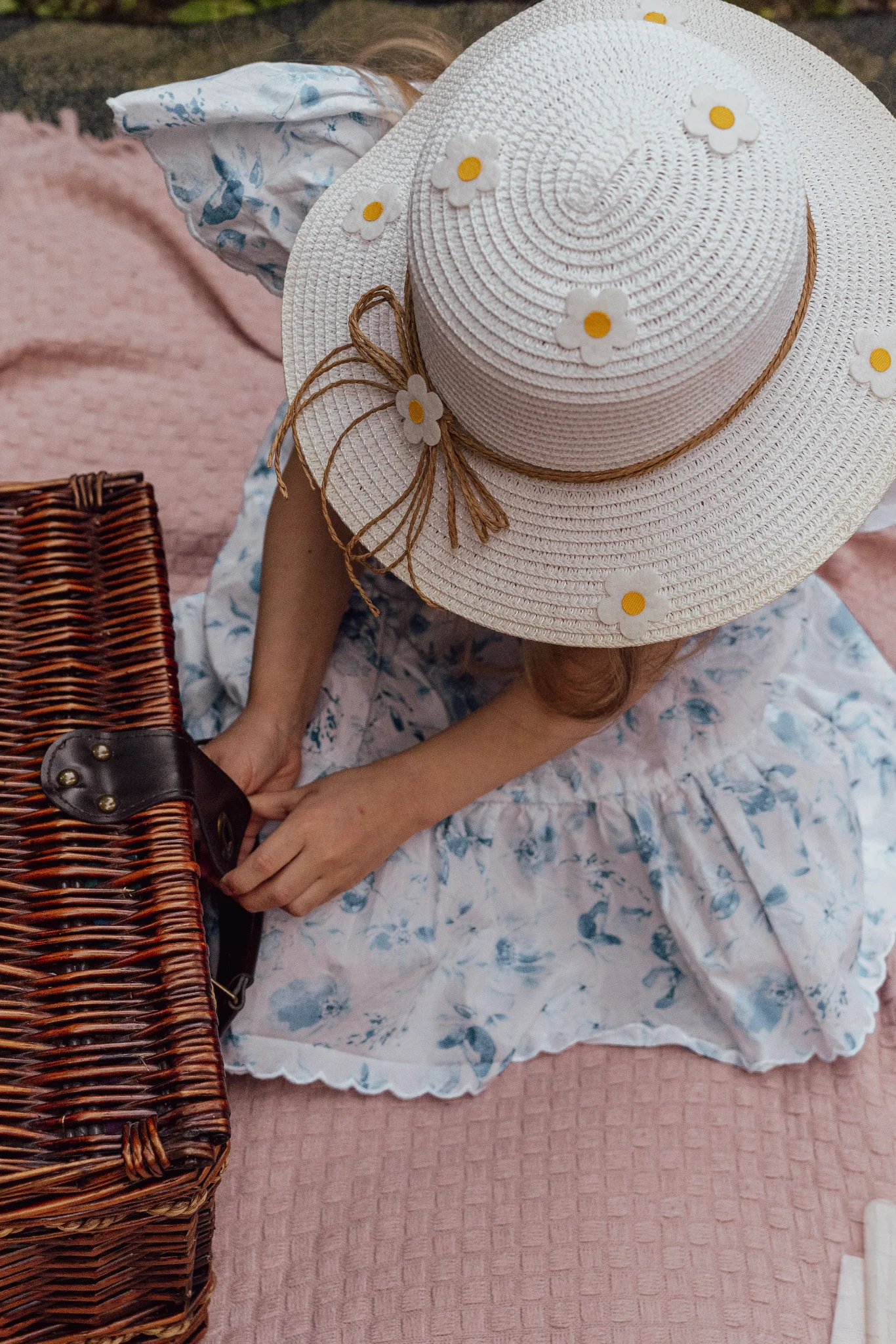 Little girl wearing a hat sitting on a picnic blanket.