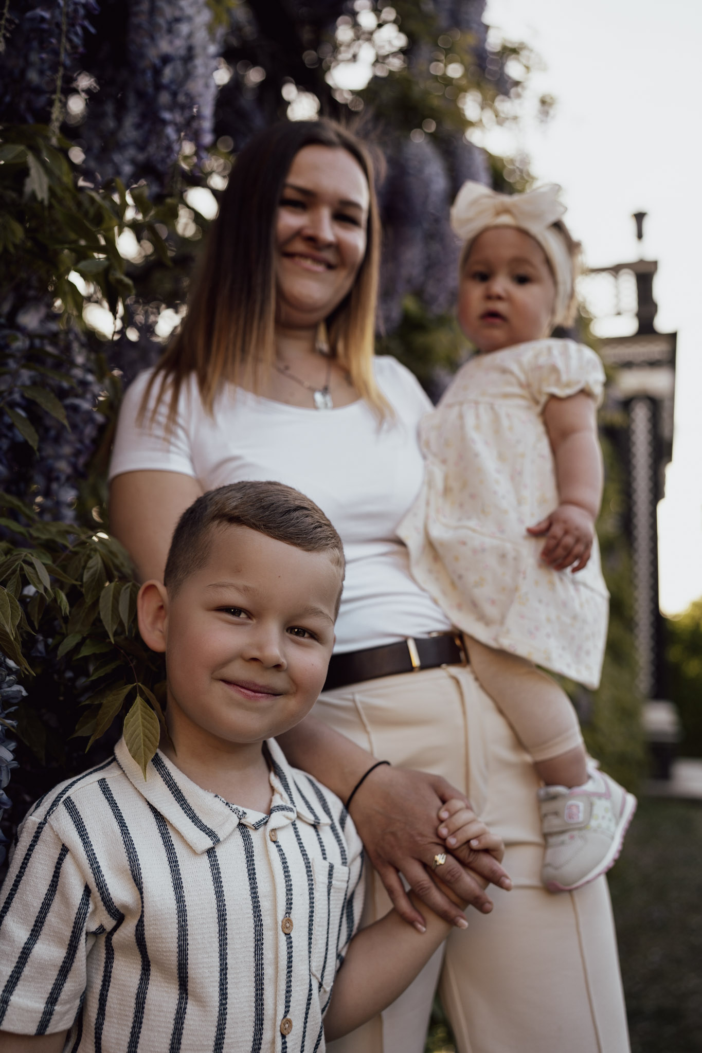 Maminka drží obě děti, dceru v náručí a syna za ruku.
